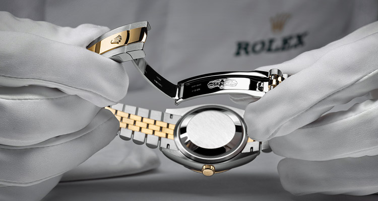 Eine Person mit Handschuhen öffnet das Faltschließen-Armband einer Rolex Uhr 