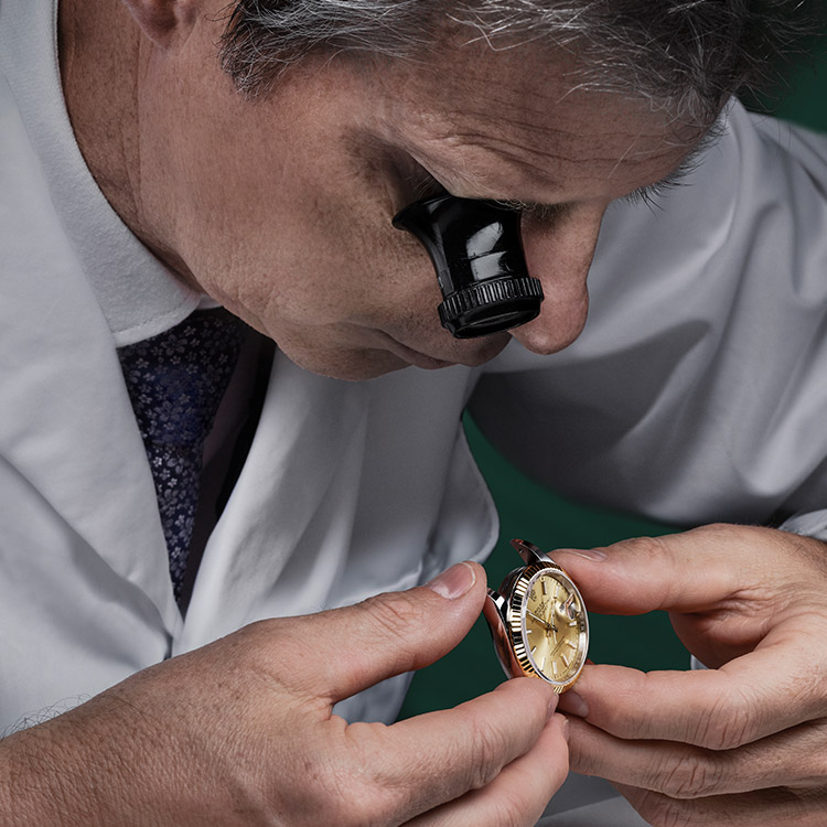 Ein Uhrmacher schaut sich durch eine okulare Lupe eine Rolex Uhr genau an