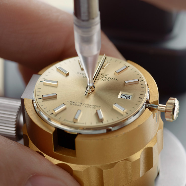 Ein Uhrmacher richtet die Zeiger auf dem Zifferblatt einer Rolex Uhr auf 12 Uhr aus