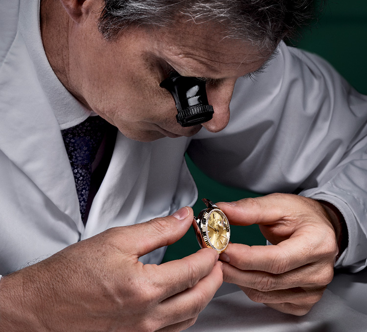 Ein Uhrmacher schaut sich durch eine okulare Lupe eine Rolex Uhr genau an