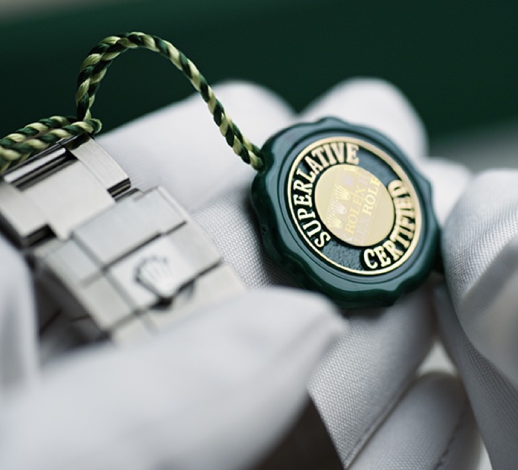 Edelstahlarmband mit Rolex Hangtag Superlative Certified von Händen in weißen Handschuhen gehalten. 