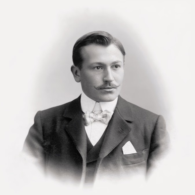 Schwarz-Weiß-Foto vom Rolex Gründer Hans Wilsdorf. Er trägt einen Anzug und eine Fliege.